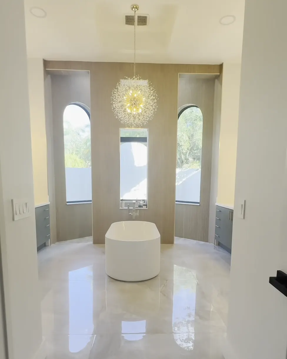 The same view finished, with a freestanding tub under three windows and a gold chandelier