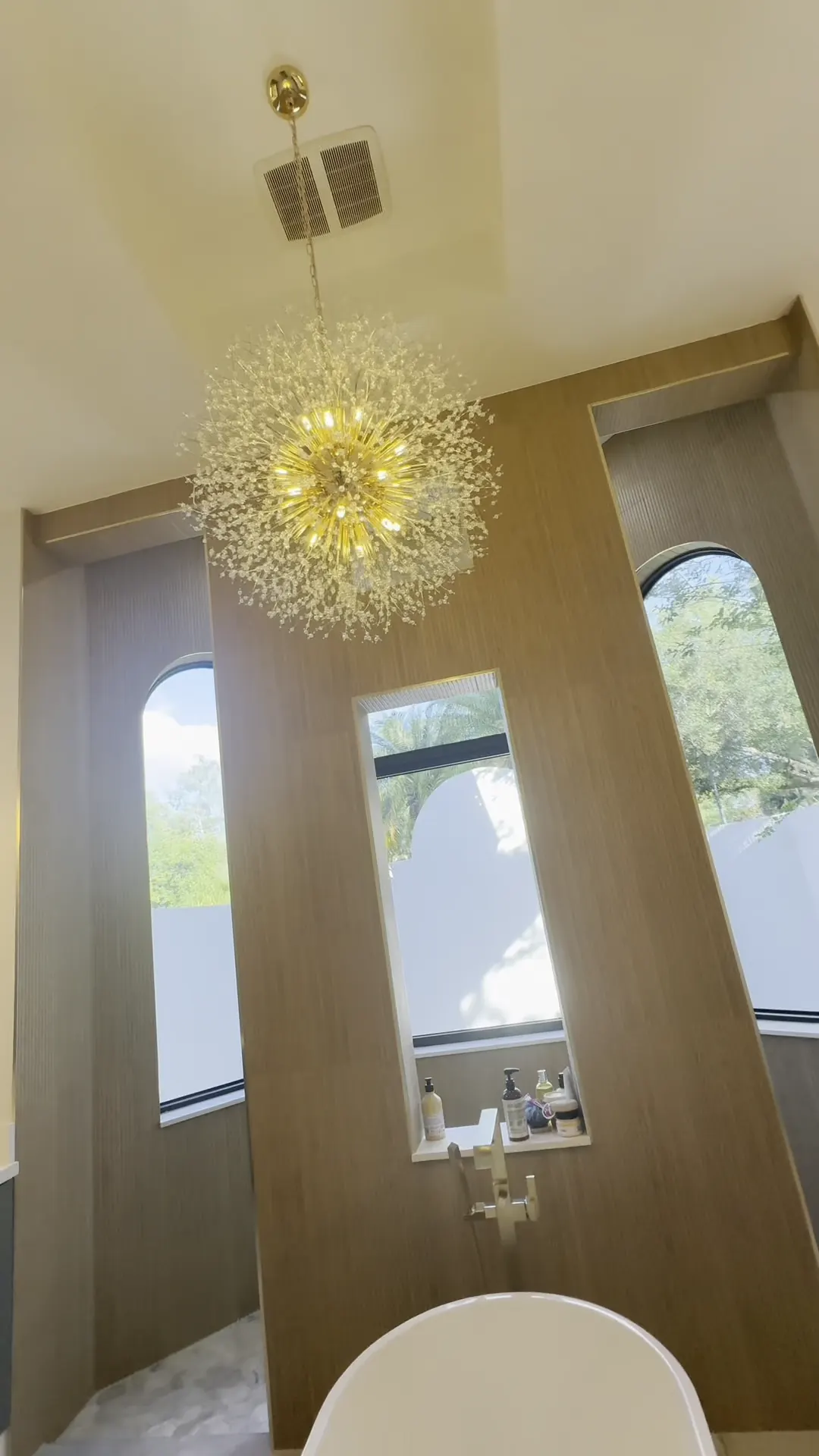 Gold starburst chandelier hanging over a freestanding tub in a bathroom with wood grain wall panels
