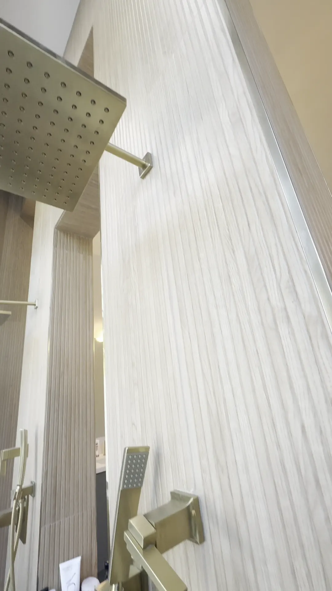 Rain shower head and brushed gold fixtures on a tiled wall