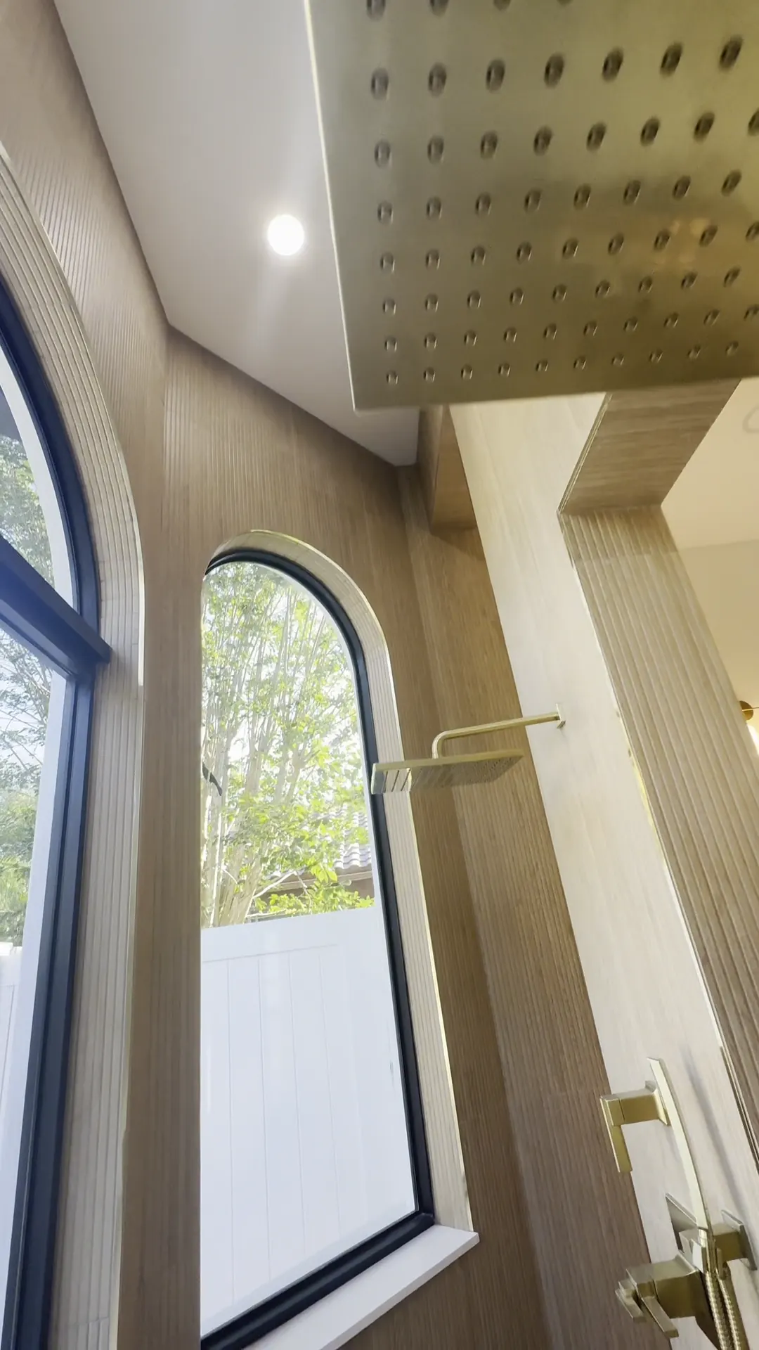 Shower with a brushed gold rain head, wood slat panels and arched windows