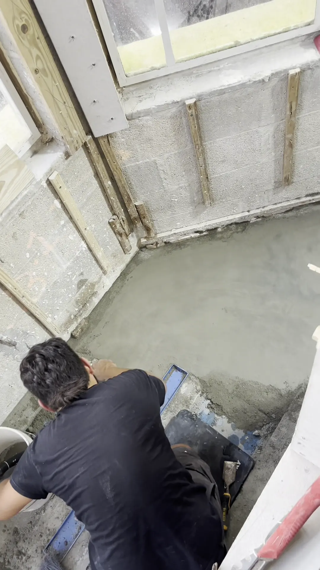 Worker kneeling to spread the mortar bed for a curved shower floor between block walls