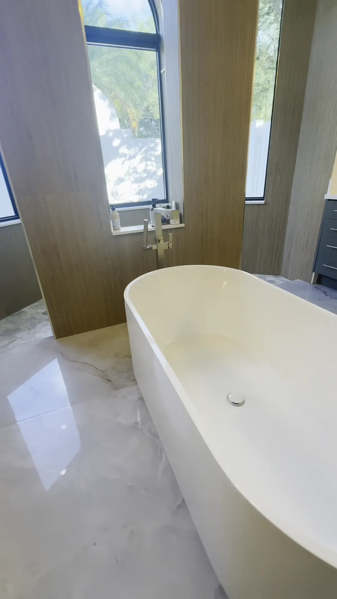 Freestanding tub in front of a wood slat wall and a tall window