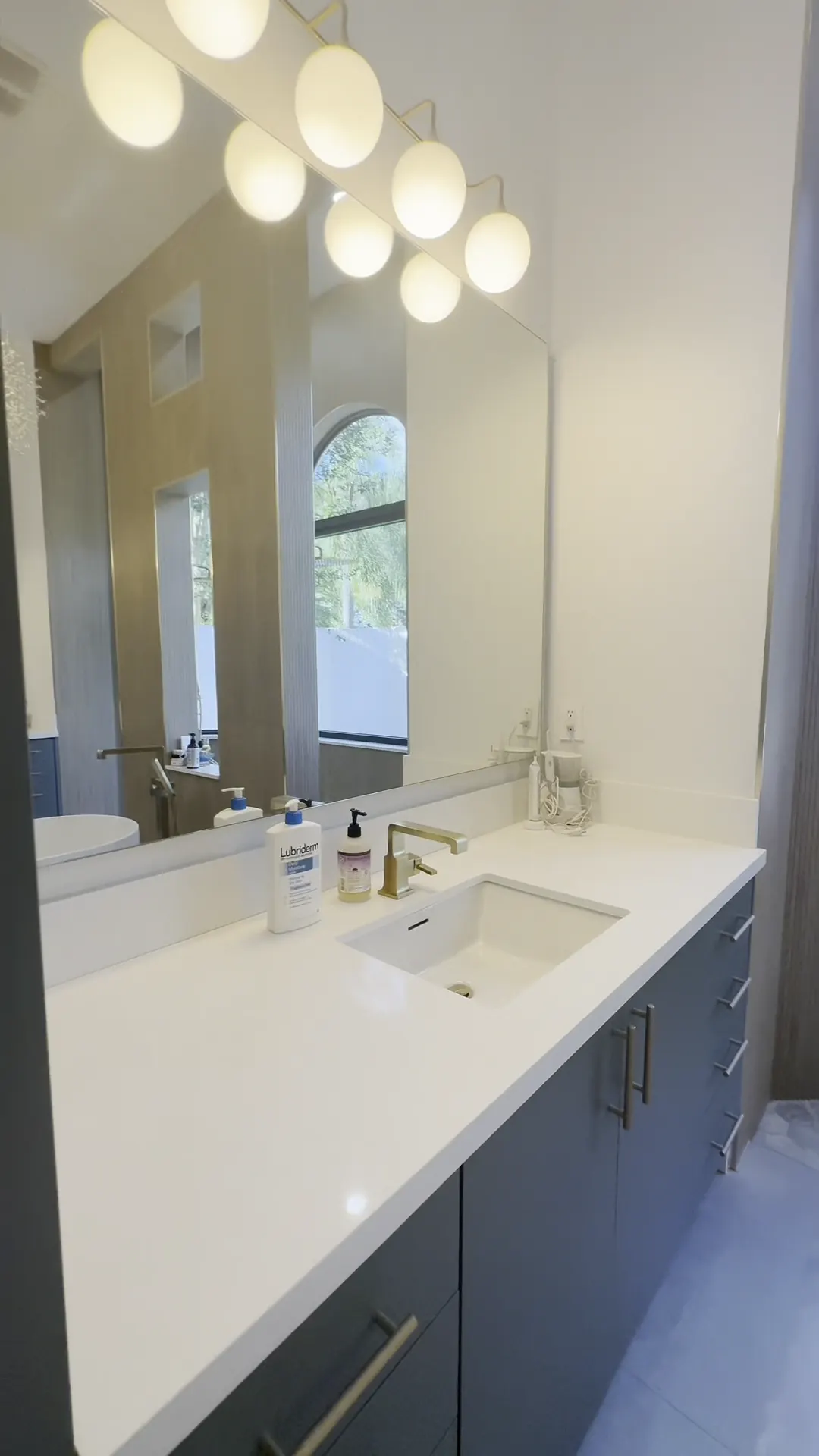 Green vanity with a white top, a round mirror and globe lights