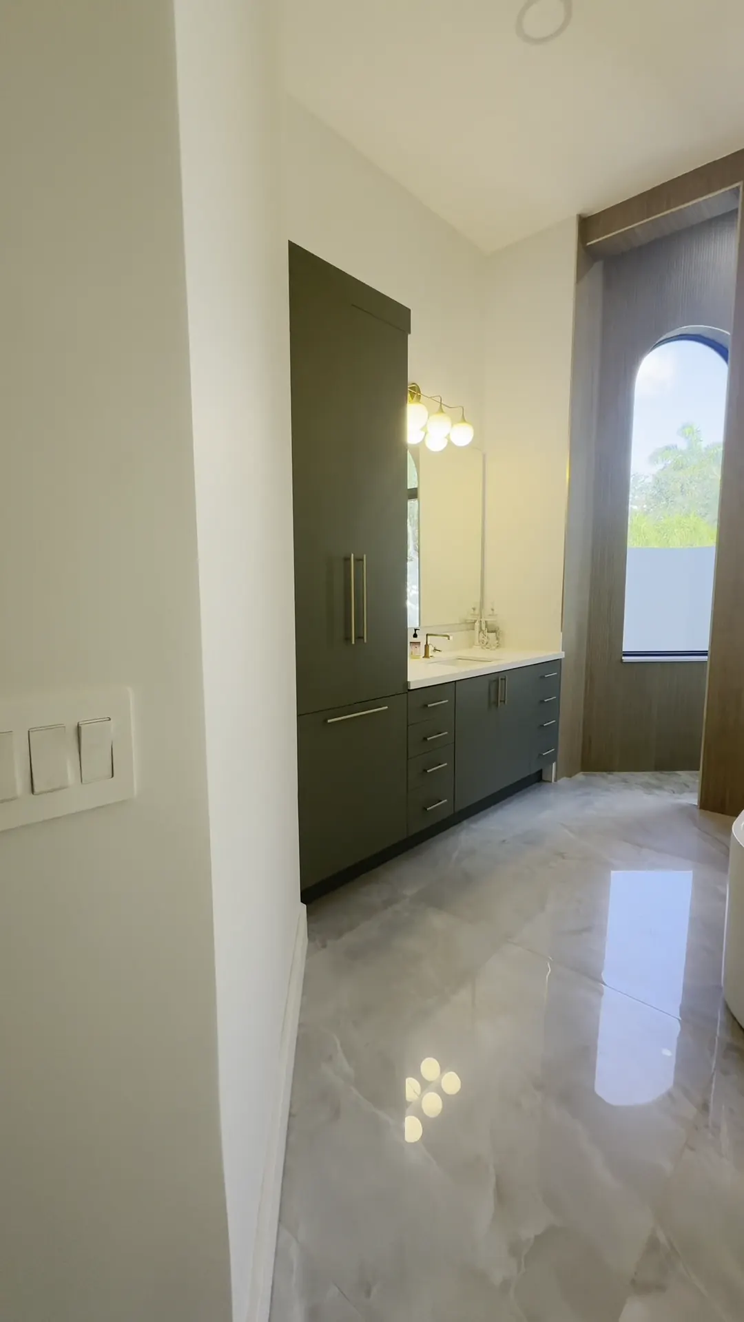 Tall green cabinet and vanity beside a window, over a glossy marble floor
