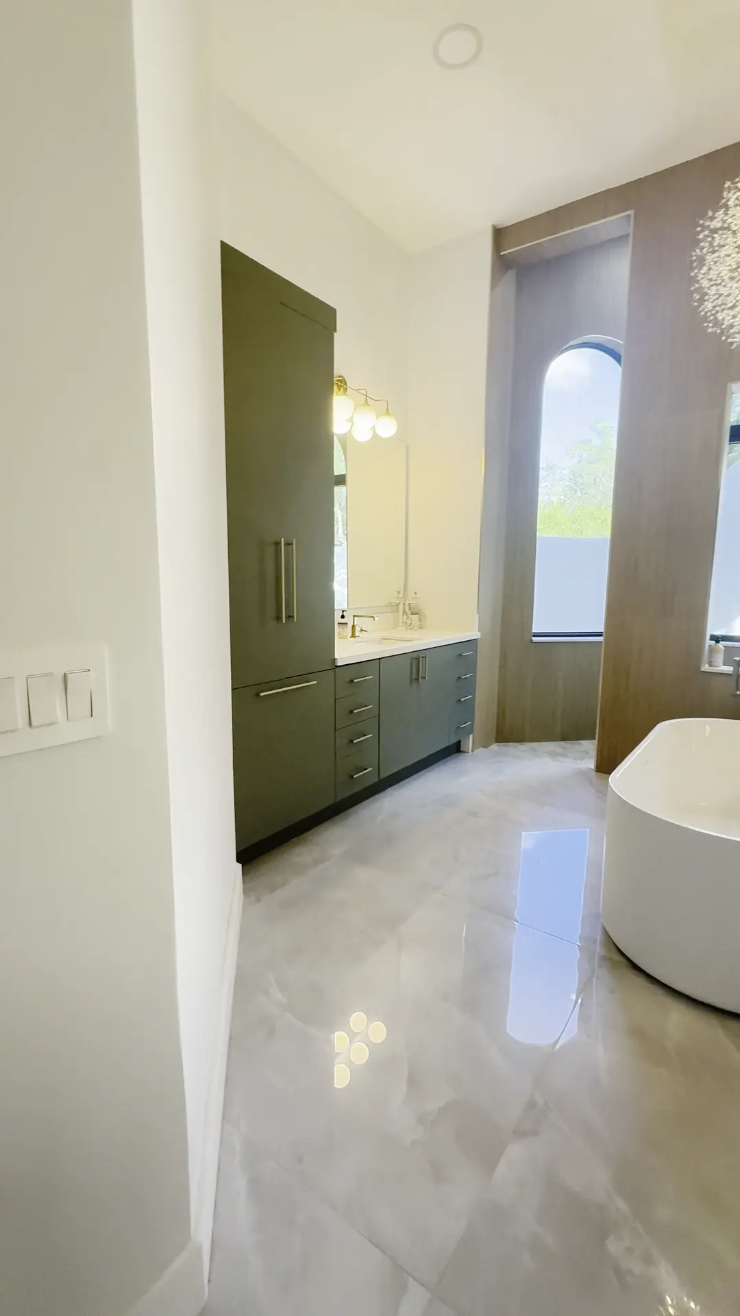Tall green storage cabinet beside a double vanity and an arched window
