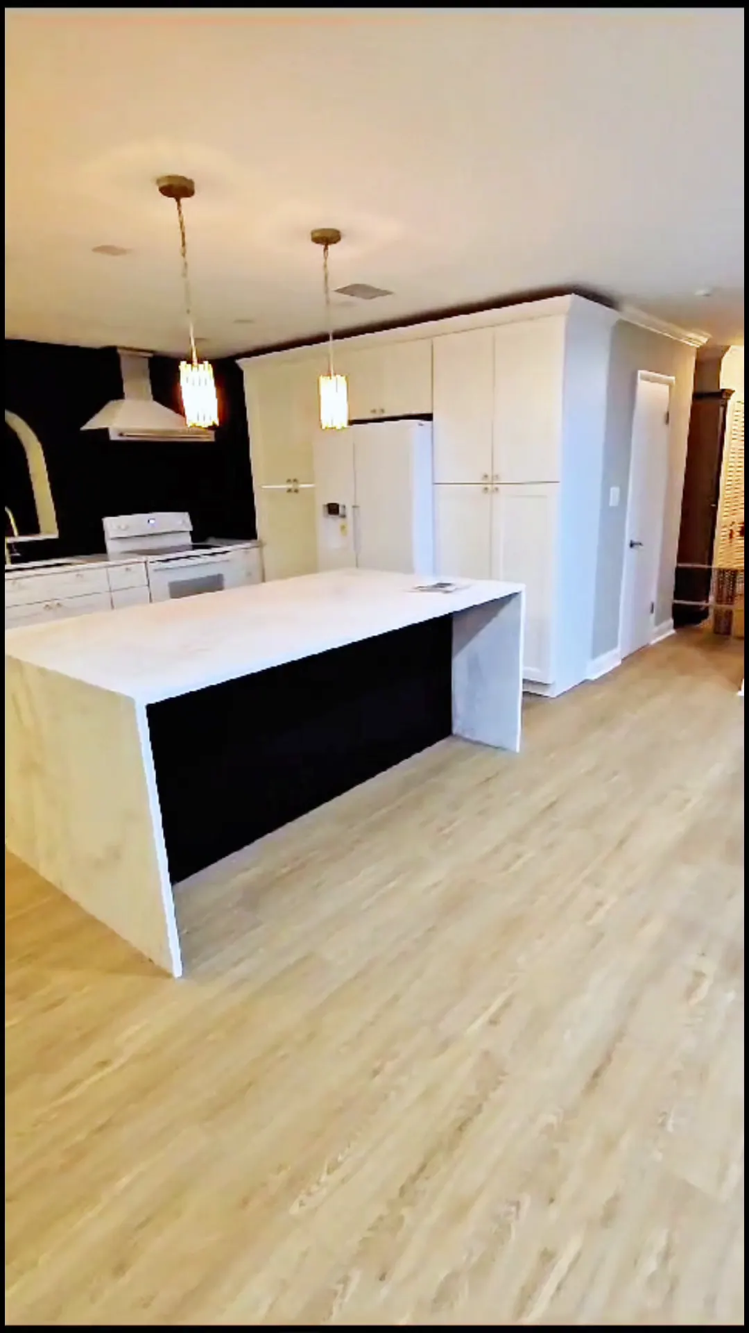 Finished kitchen with a waterfall island, pendant lights and a black accent wall