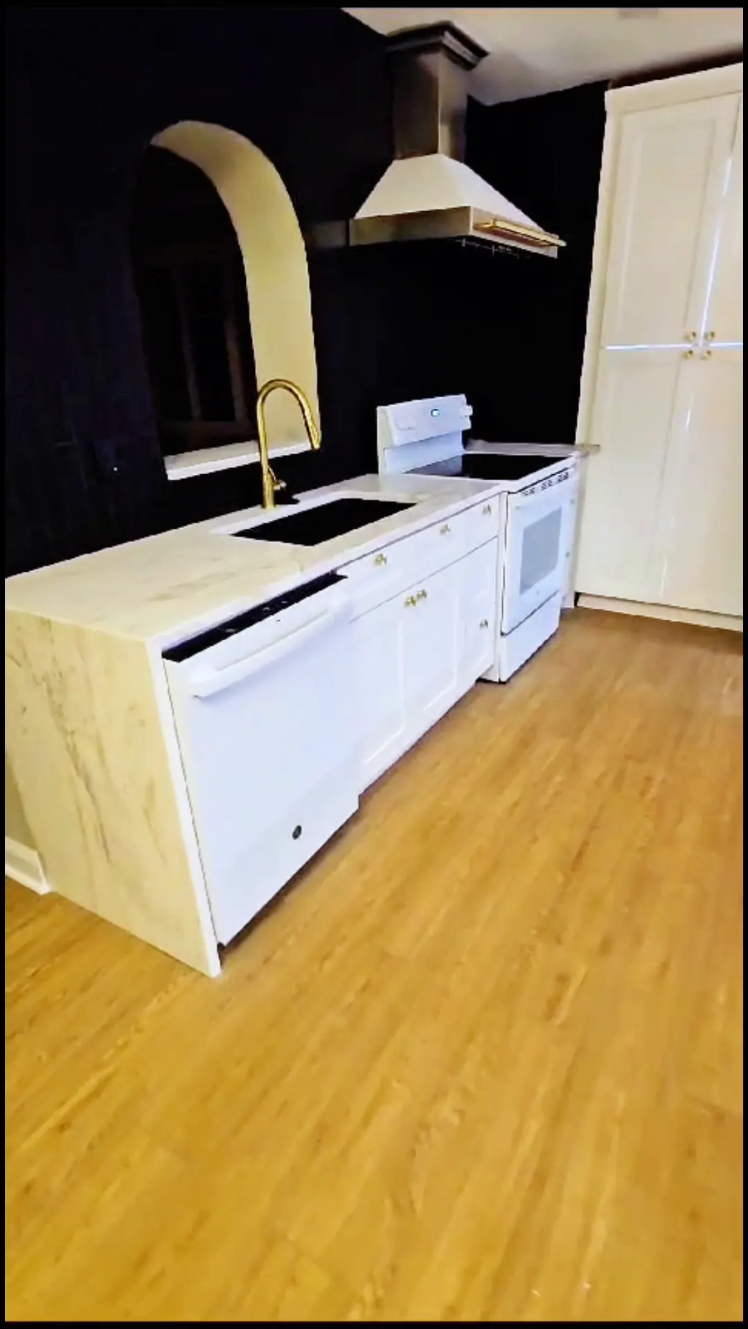 White kitchen run with a stone counter, a gold faucet and a range under a white hood