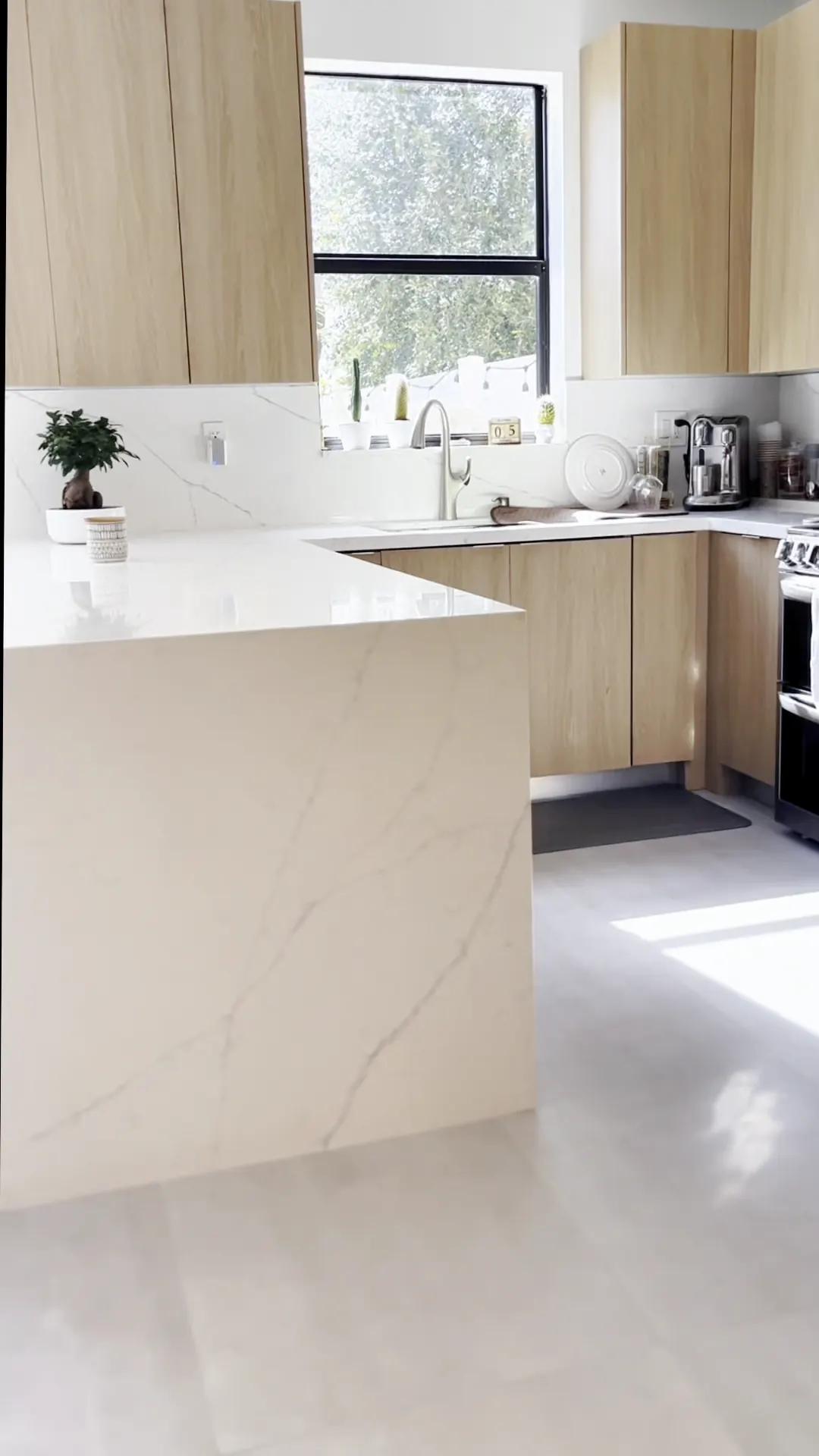 White waterfall island in front of a window and light wood cabinets
