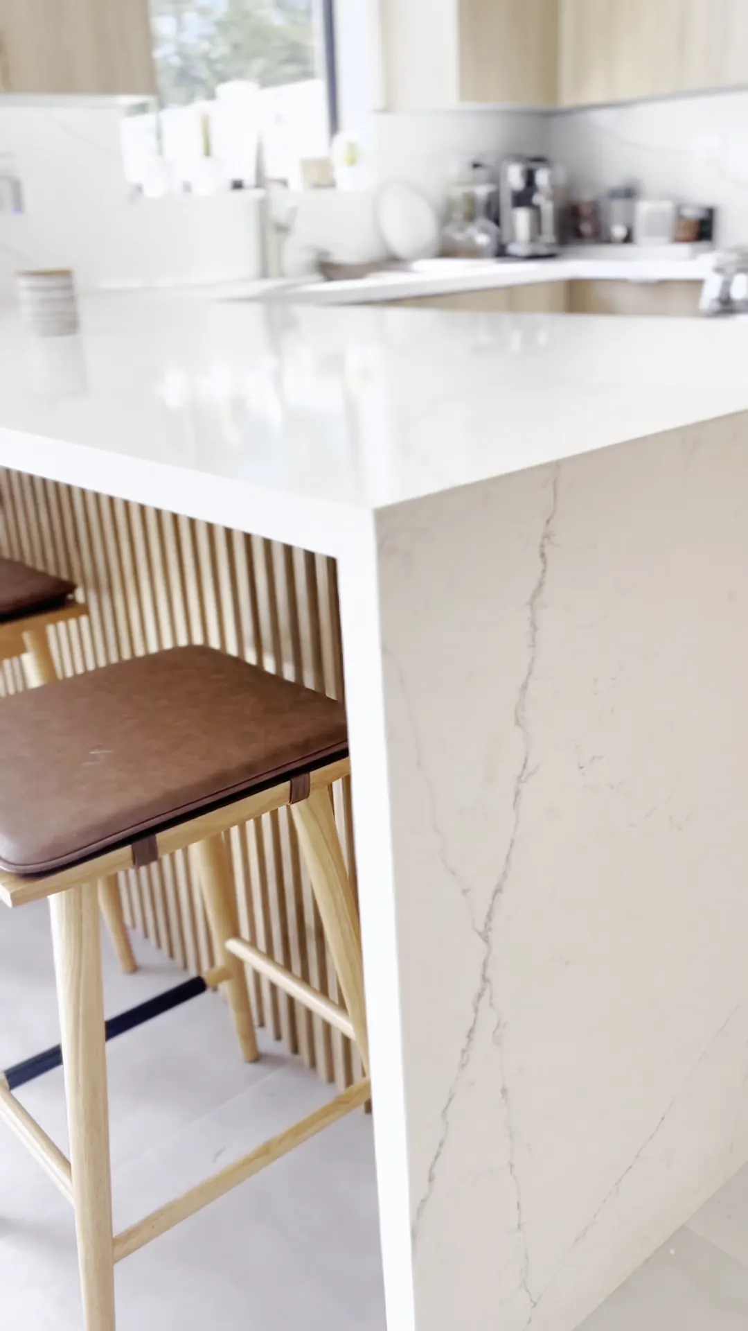 Waterfall counter edge with wood slat panels and leather bar stools