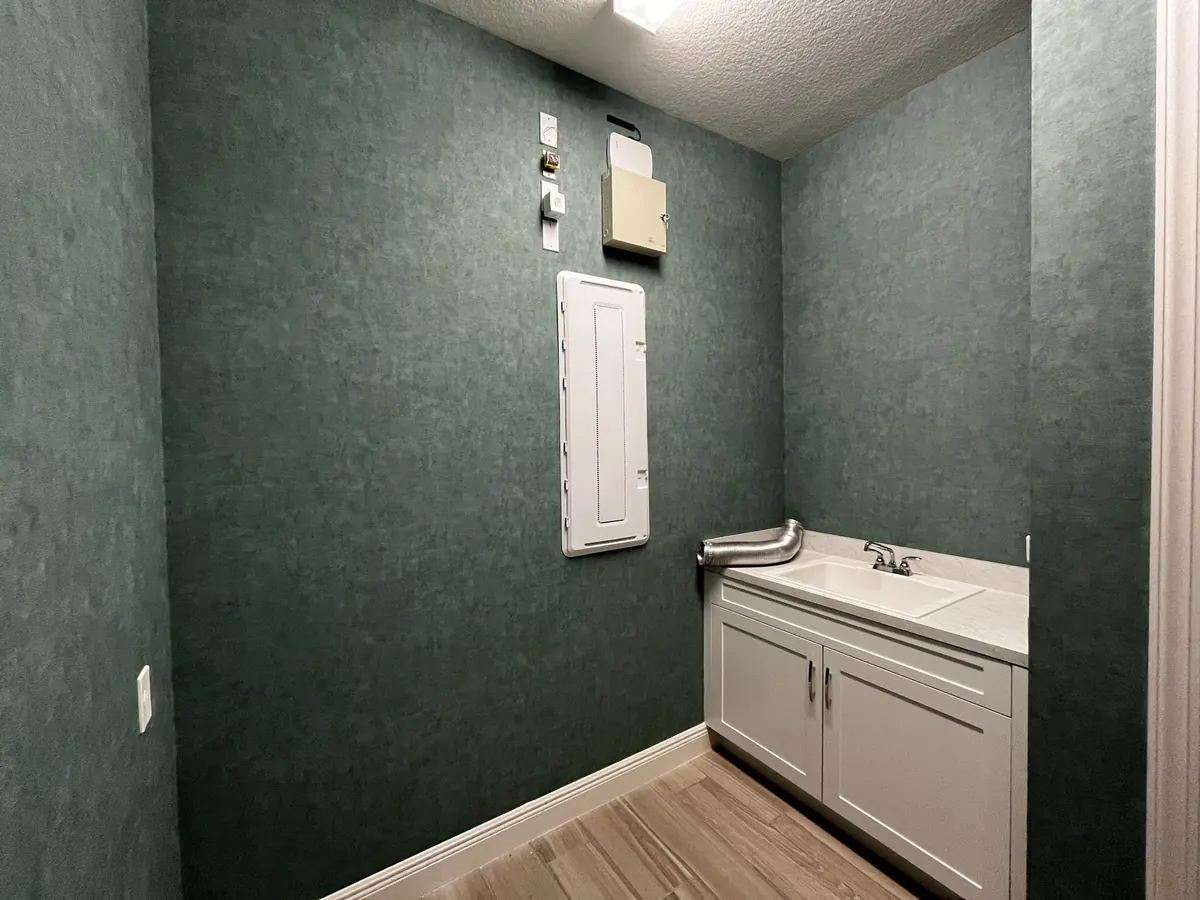 Laundry room with textured green wallpaper, a white cabinet and a utility sink